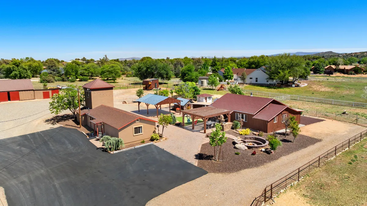 The exterior of the main house at dusk, featuring an outdoor gathering area, landscaped garden, and an inviting patio space. The mood is serene, with the potential for stargazing and children playing in the yard. The open sky and clear sightlines evoke the experience of stepping outside to enjoy Arizona’s magical nights.