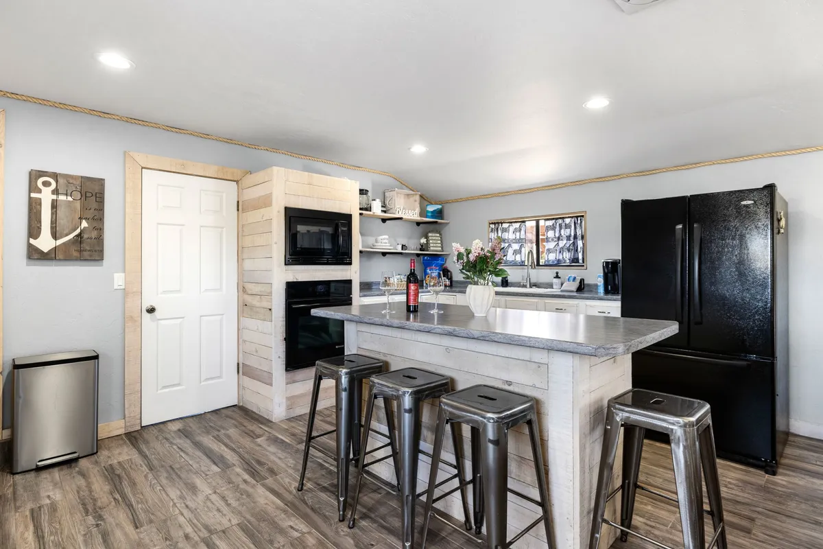A warm and inviting kitchen-dining area, highlighted by a central island, stainless steel appliances, a floral centerpiece, and wooden cabinetry. The space is designed for cooking, sharing meals, and engaging in casual conversations over coffee.