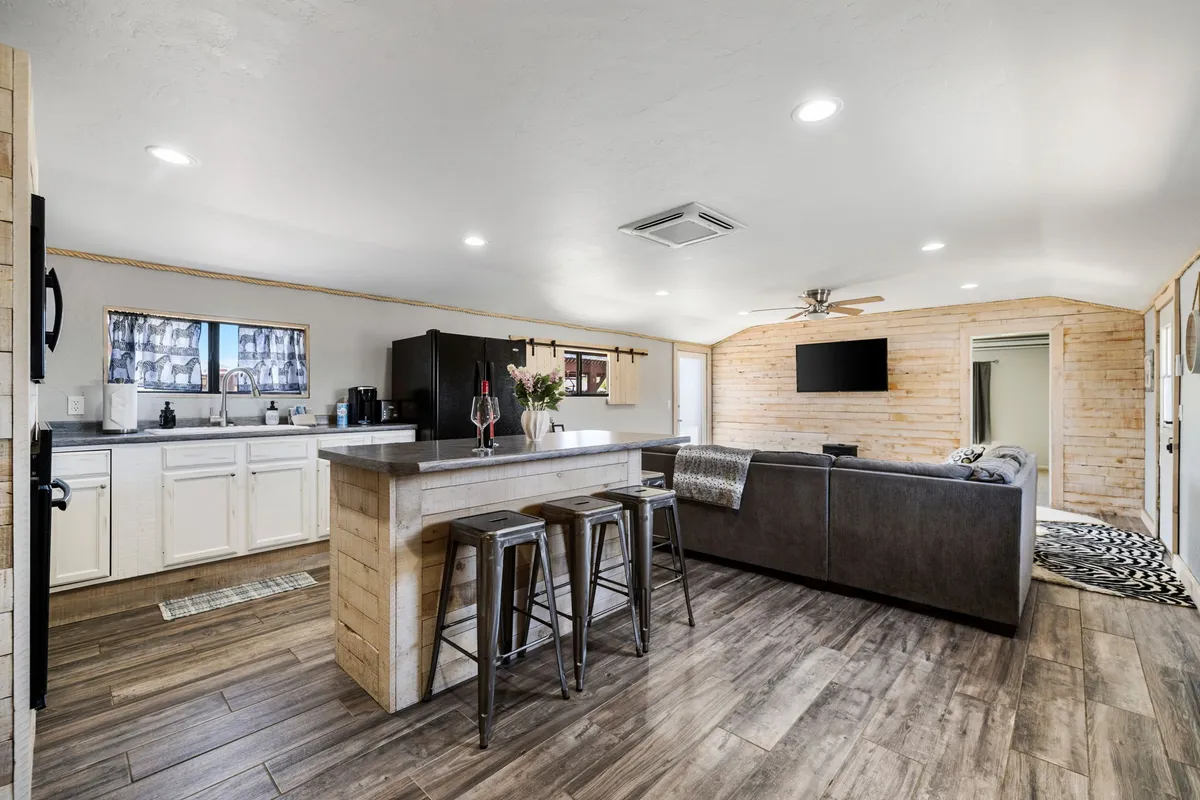 A modern yet cozy kitchen and living area with a kitchen island, contemporary seating, and wooden wall accents. The connected layout encourages seamless movement between preparing food and relaxing with friends or family.