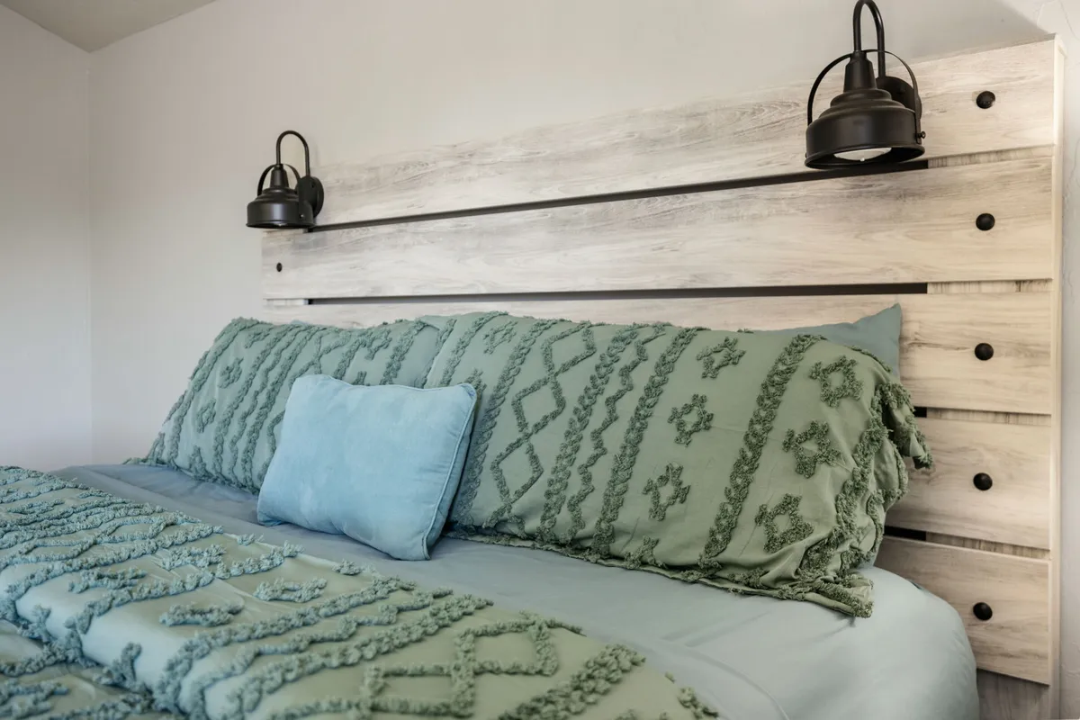 A serene bedroom scene featuring textured bedding, a wooden headboard, and industrial-style light fixtures. The ambiance is warm and inviting, perfect for winding down after a long day. The soft linens and calm, neutral décor create a comfortable and restful environment, with enough space for couples or quiet moments.