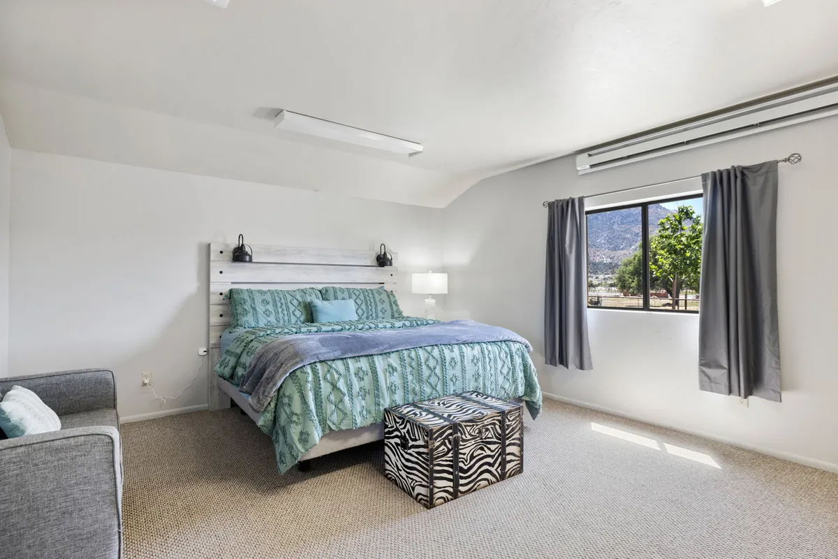 A cozy bedroom with decorative bedding, a zebra print ottoman, and a window offering a scenic view. The room feels relaxed and snug, with natural light streaming in and a nook by the window that’s ideal for reading or enjoying the view. The décor brings a gentle nod to nature and peacefulness.