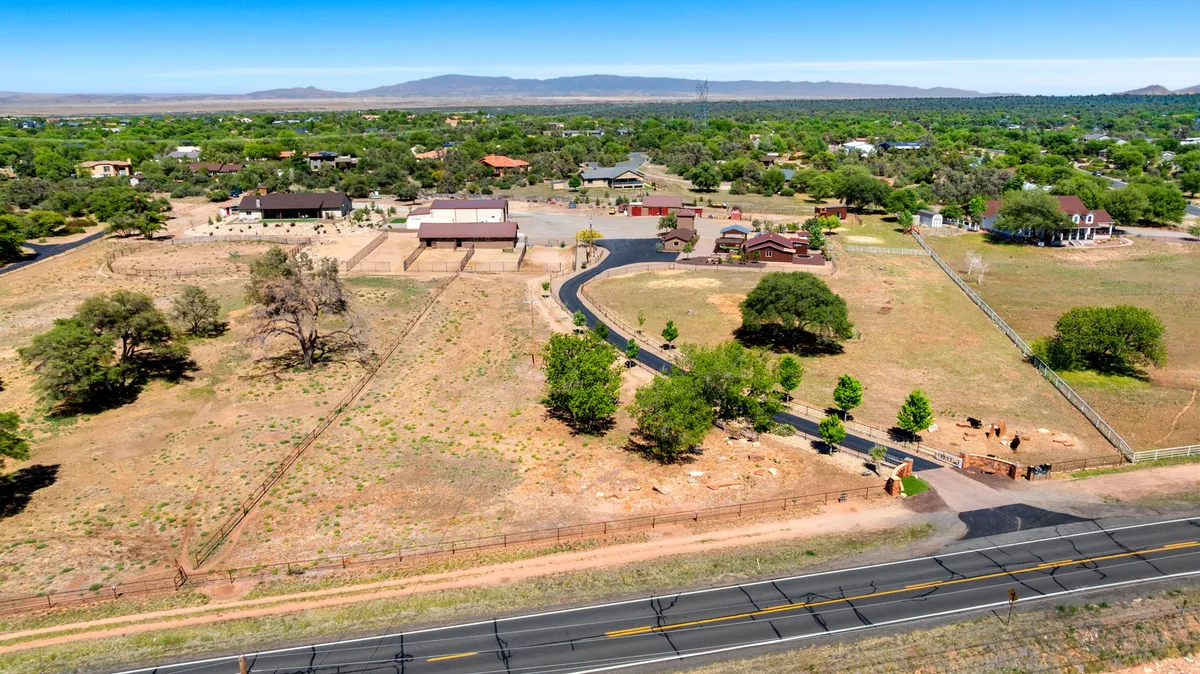 A wide-angle exterior shot of the ranch property, showing the main house, an inviting roadway, lush greenery, and fenced areas ideal for activities like walking, horseback riding, and stargazing at night. The open expanse and natural landscaping suggest a serene yet adventurous environment.